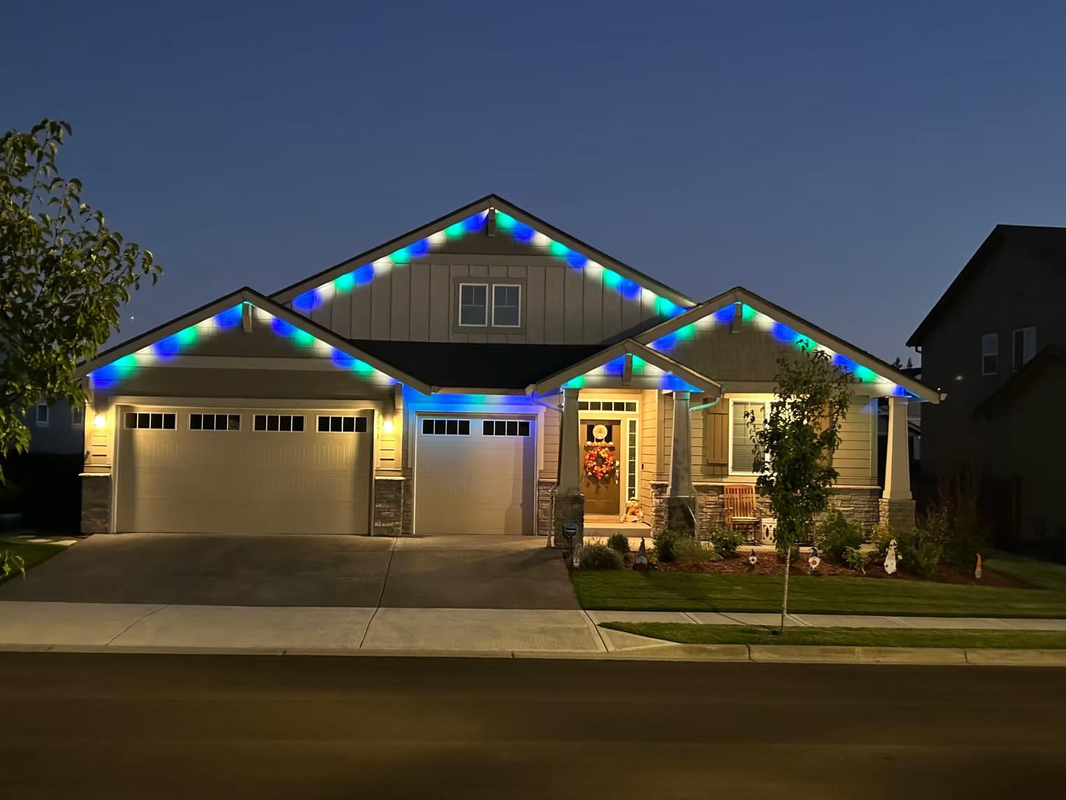 Blue and green lights along the roof peaks of a home viewed from the street