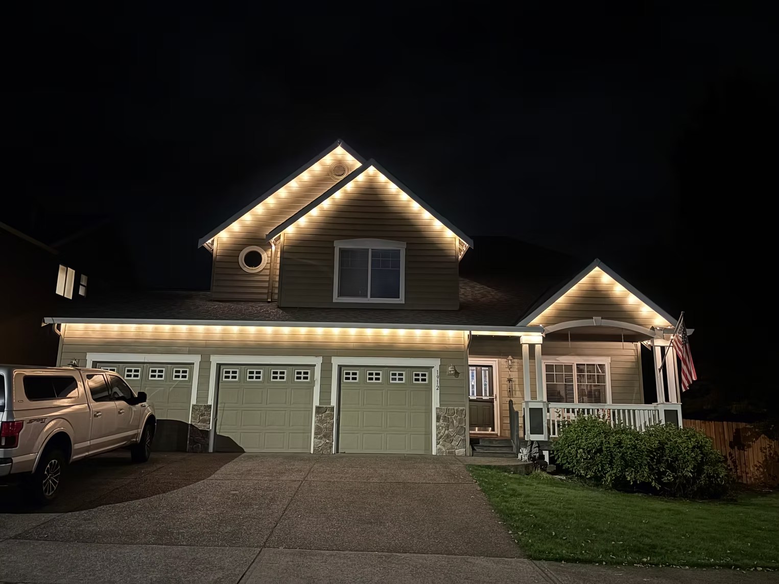 Warm-white lights outlining a two-story home and its front porch at night