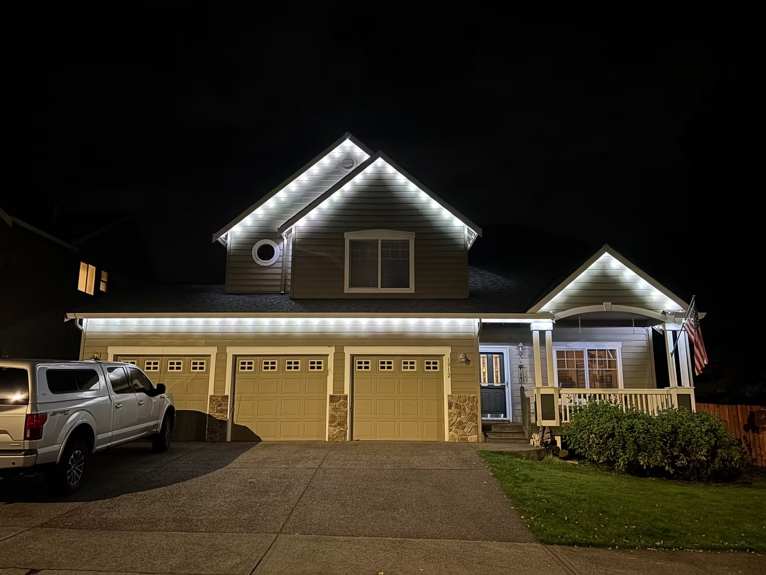 White lighting across a two-story home’s garage and upper roof peak