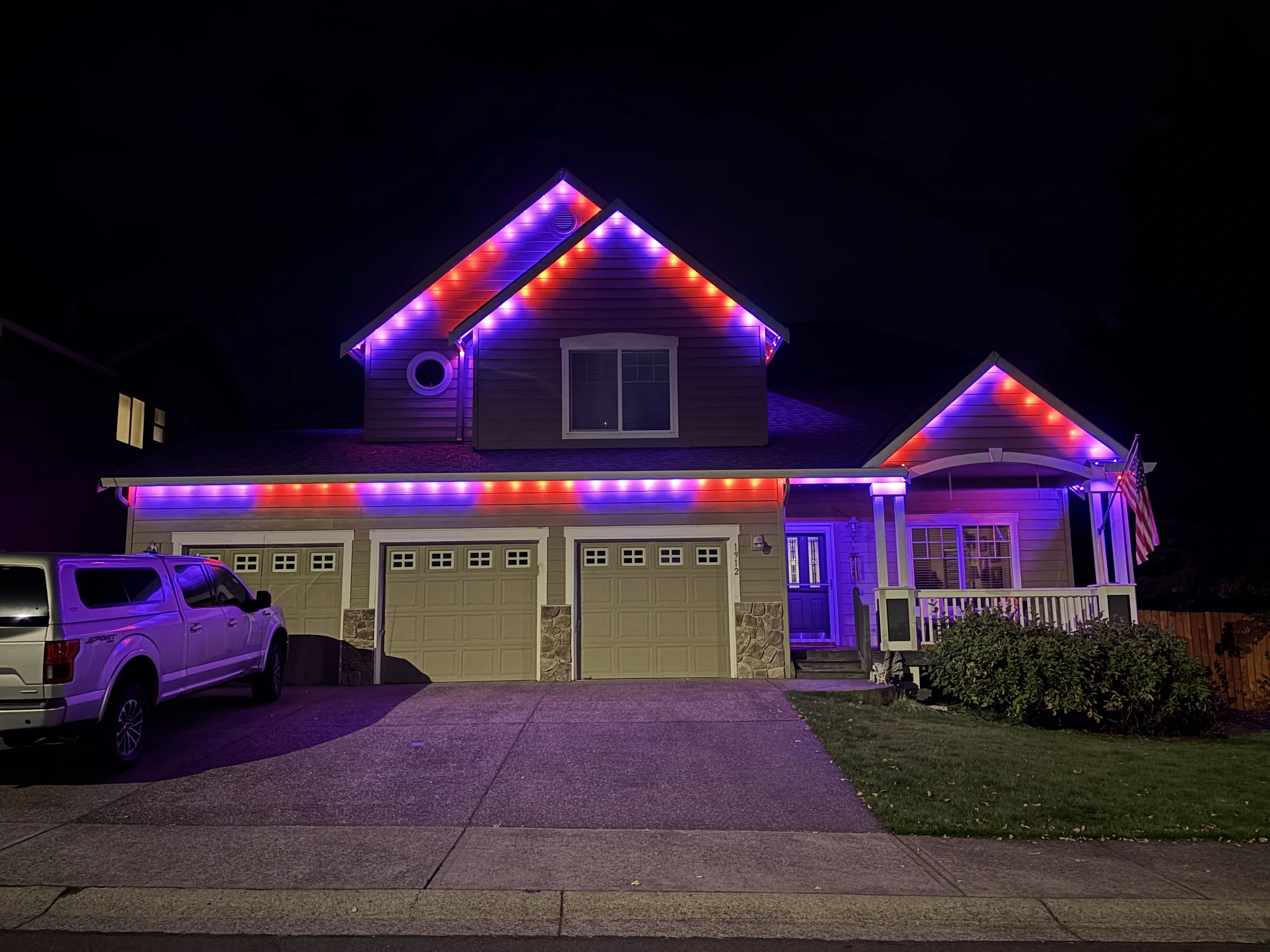 Purple and red lights across a home’s roof peaks, garage and front porch at night