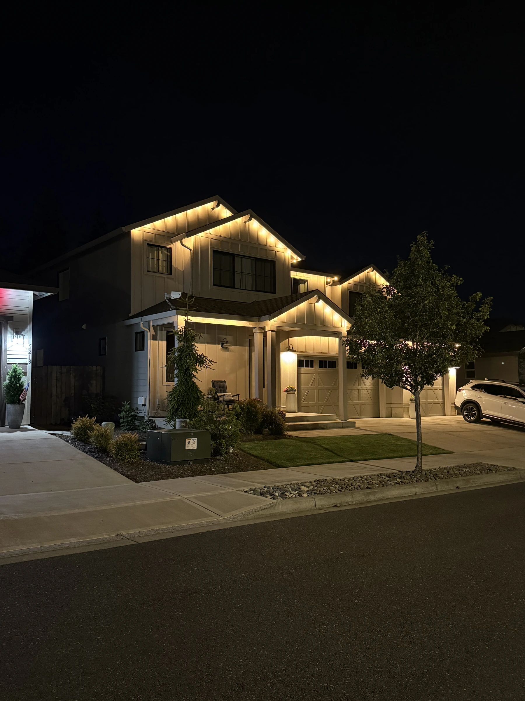 Warm-white roofline lights on a two-story home, viewed from the sidewalk at night